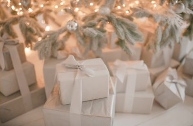 Mehrere kleine, weiß verpackte Weihnachtsgeschenke liegen ordentlich unter einem warm leuchtenden Tannenbaum, der eine festliche und ruhige Weihnachtsstimmung erzeugt.